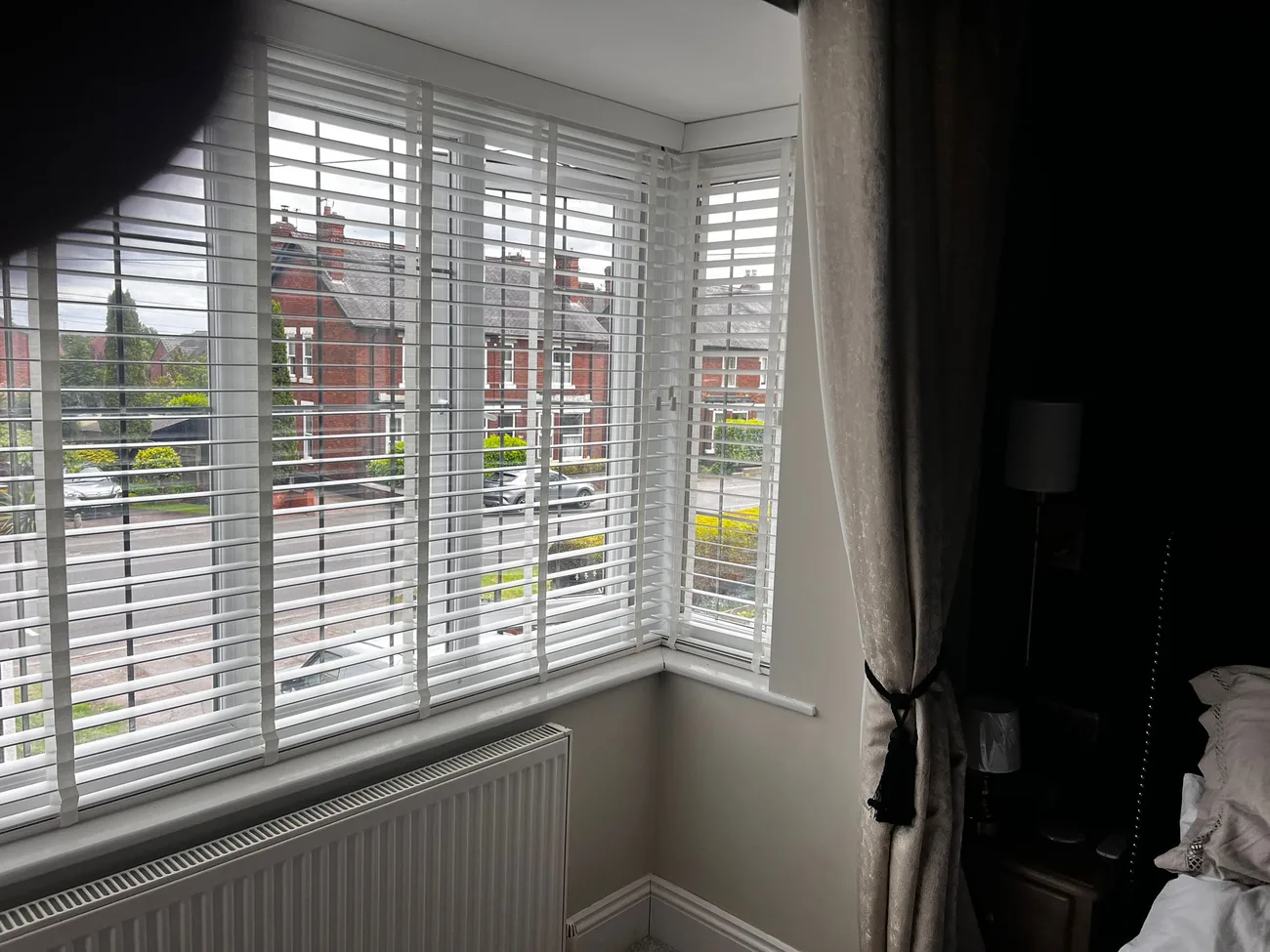 White slatted blinds fitted across a bay window, viewed from one side