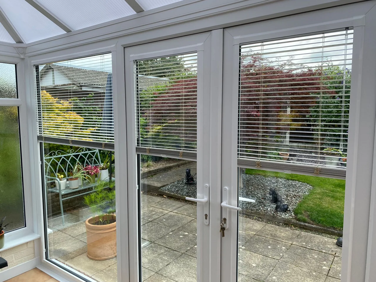 Slatted blinds fitted within white conservatory door frames overlooking a garden