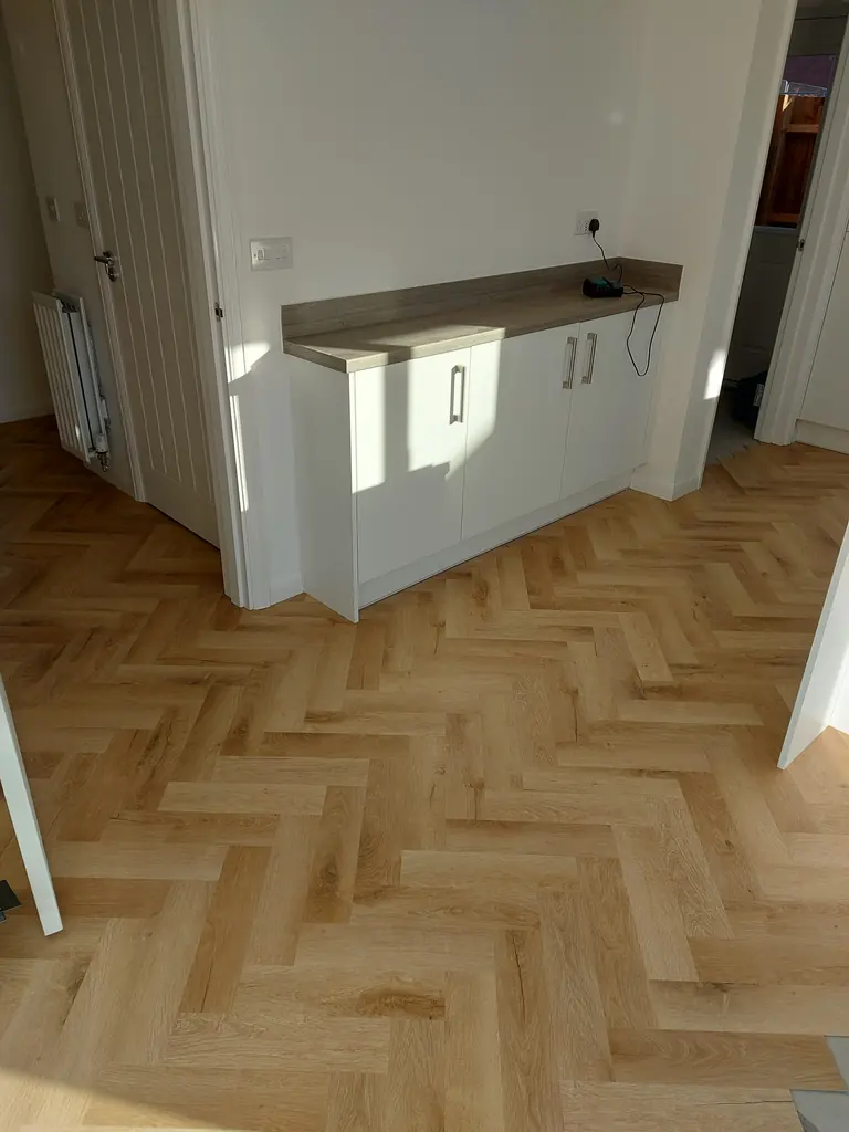 Completed warm wood-look herringbone floor around kitchen cabinets and doorways