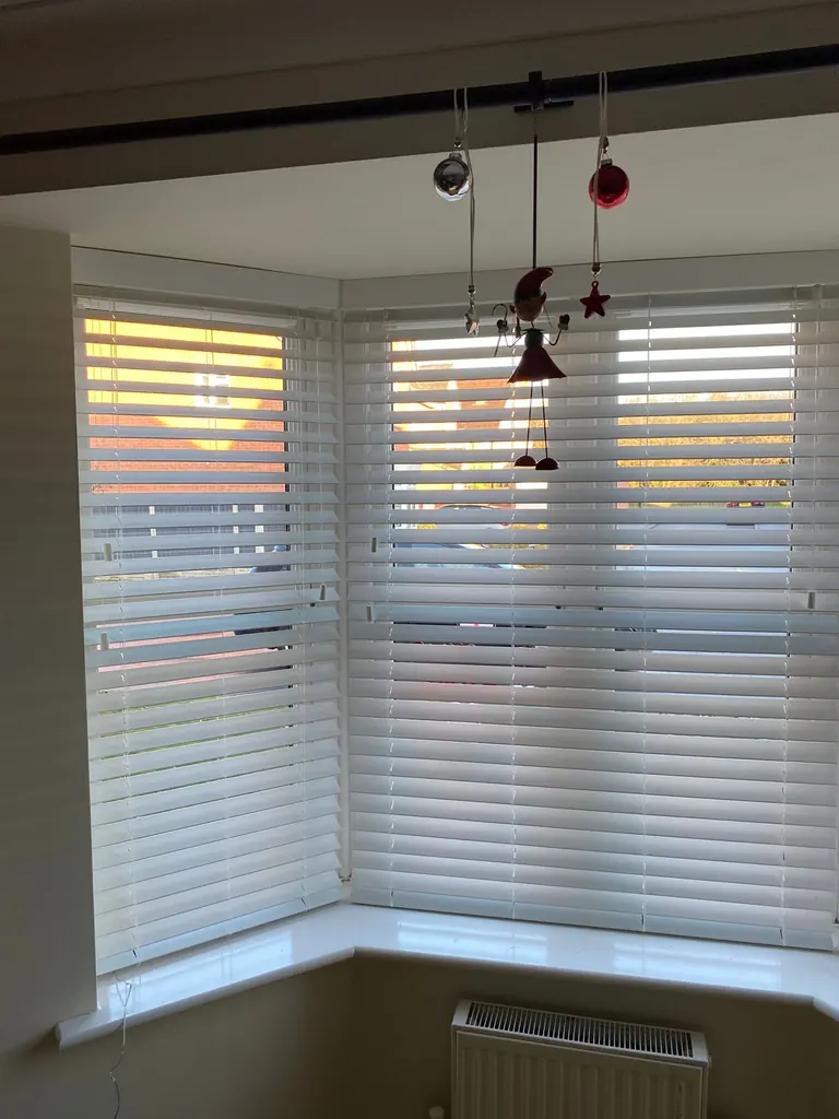 White slatted blinds fitted across a bay beneath pendant lights
