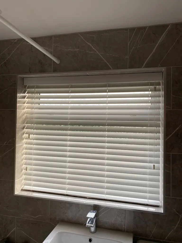 White slatted blind fitted above a basin in a tiled room